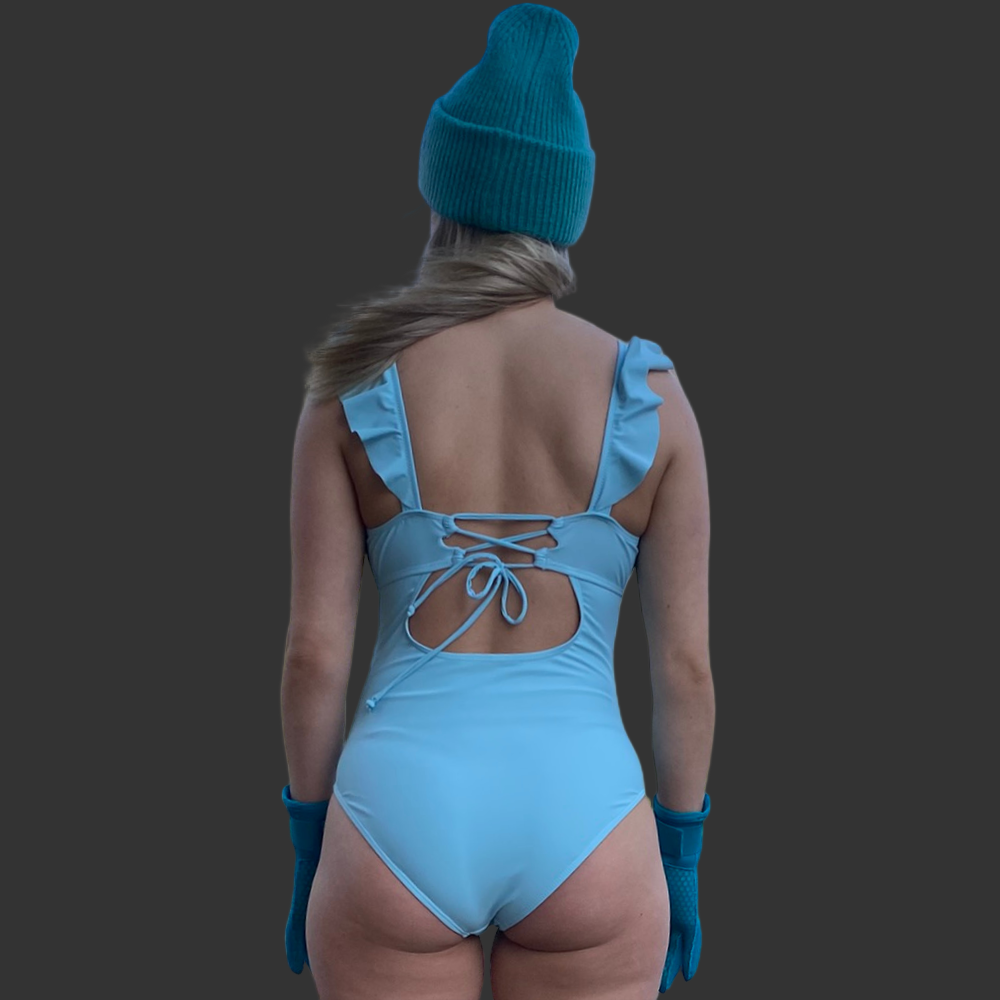 En dame som har på en himmelblå badeddrakt med volanger og snøring i ryggen som tilbehør turkis lue og neopren hansker